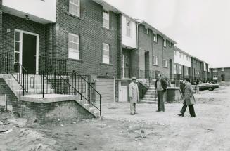 Exterior view of two-storey, flat-faced brick townhouse complex with cement front steps and gar…