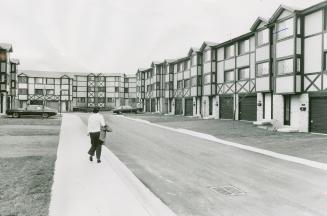 Row of three-storey attached townhouses with Tudor-style dark accent beams. Driveways lead to g…