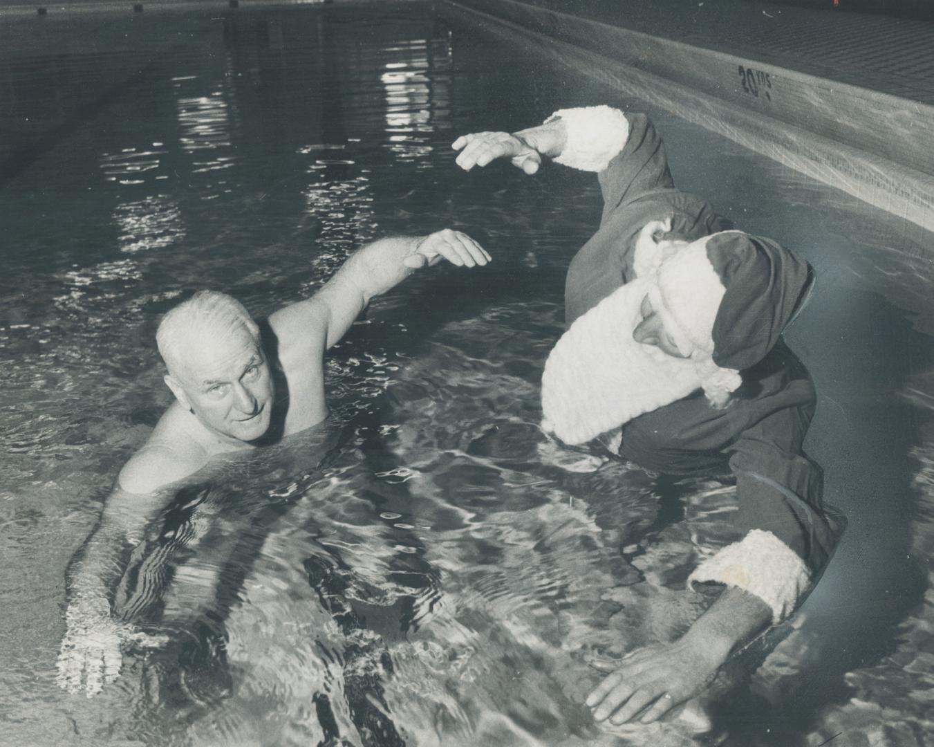 Santa is in the swim. Santa Claus, alias John Baun, gets swim instruction from Gus Ryder in case of mishap when he arrives by canoe for crippled child(...)