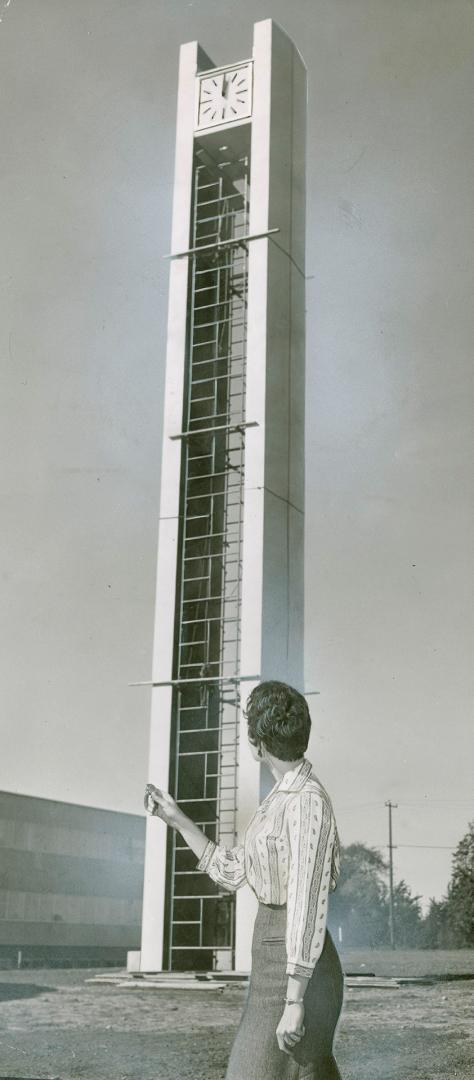 Woman points toward a very tall, narrow tower constructed of geometric shaped rungs supported b…