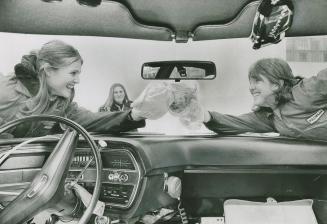 Driver's seat view from car interior of steering wheel, dashboard, and two girls reaching acros…