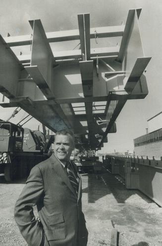 Biggest In North America, Joe Botting, sales manager of Dufferin Steel, Toronto, stands under one of four 30-ton steel support forms built for new plant of crown-owned Polymer Corp. at Milton, Ont.