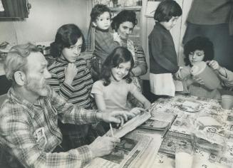 Emmauel Bourdos, whose take-home pay as a hospital orderly is about $110 a week, helps the two eldest of his six children with their homework as the family gathers around the table. From the left are Bourdos, Photini, 11, Margaret, 10, Mrs. Bourdos holding Dino, 2, Tina, 5, and Bessie, S. Bourdos is one of 6,000 Metro hospital workers who are preparing to risk the consequences of an illegal strike to get a decent wage comparable to that in similar work.