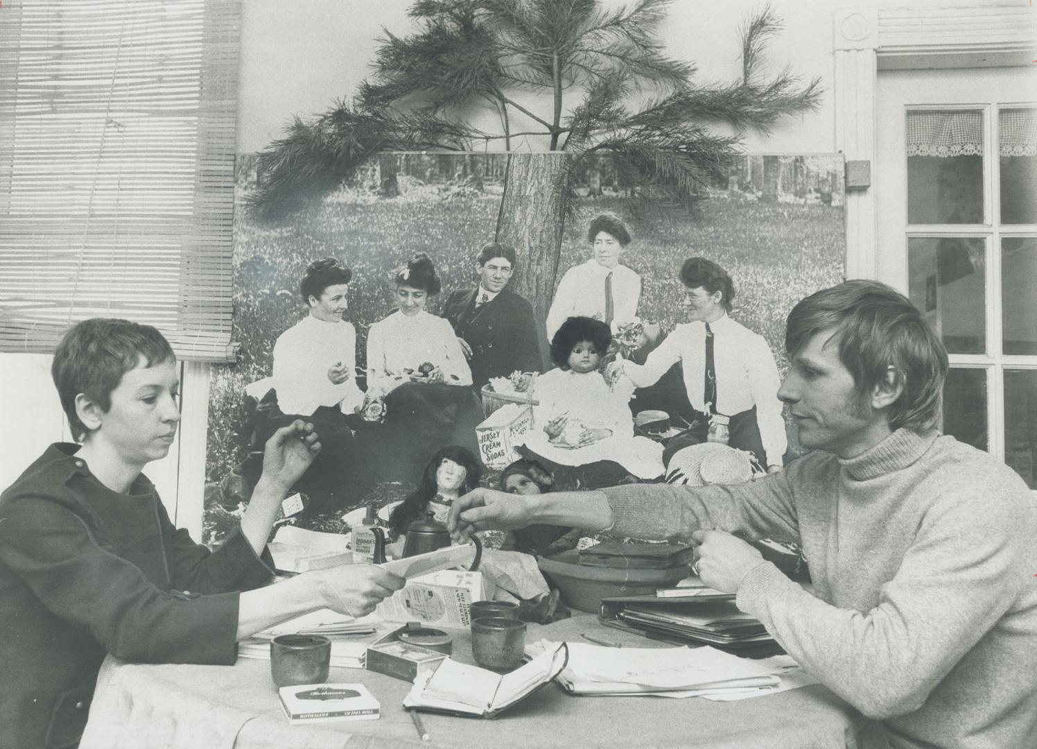 Mr. And Mrs. Willie Cadot have coffee at the dining room table in their townhouse. On wall is super enlargement of old negative, one of many collected by Cadot. Mrs. Cadot has added her to the photograph by moulding a papier-mache head on one of the figures