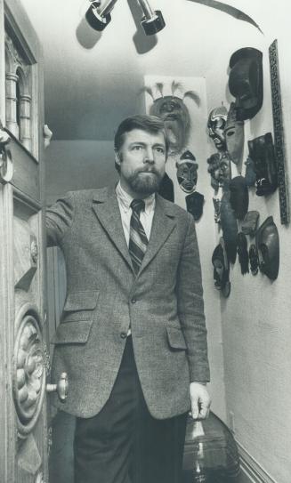 In his rosedale home, builder Hugh Conover stands before a collection of primitive masks from native Indian, Mexican and African sources. The antique door is one he bought from wreckers and installed in duplex the family bought.