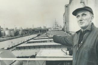 Shipkeeper Bill Cook stands on the deck of the Go one of the two ships he keeps an eye on during the wi daily inspections to check that everything is shipshap sister ship, the James Norris, are the largest grain carries now wintering in Toronto harbor. Cook receives $575 a month for keeping both ships. He lives rent-free aboard the Leitch, in the chief cook's room. [Incomplete]