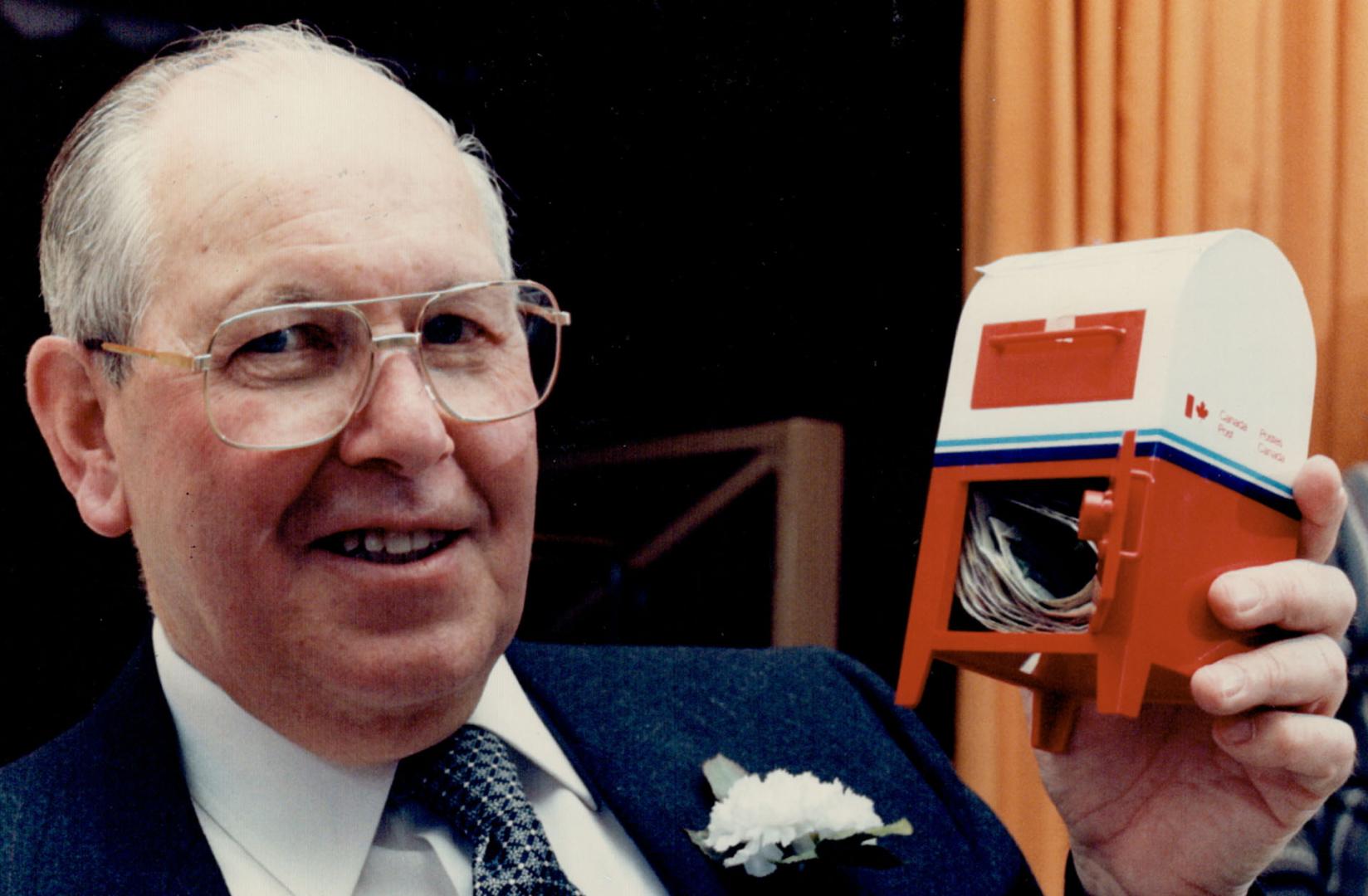 Parting gift: Retiring postman Bob Cooper holds a miniature mailbox filled with money given to him by residents on his route in the Keele St. Eglinton Ave. area on the weekend. About 75 neighbors turned out for the retirement party for Cooper, who has a delivered their mail for 32 years.