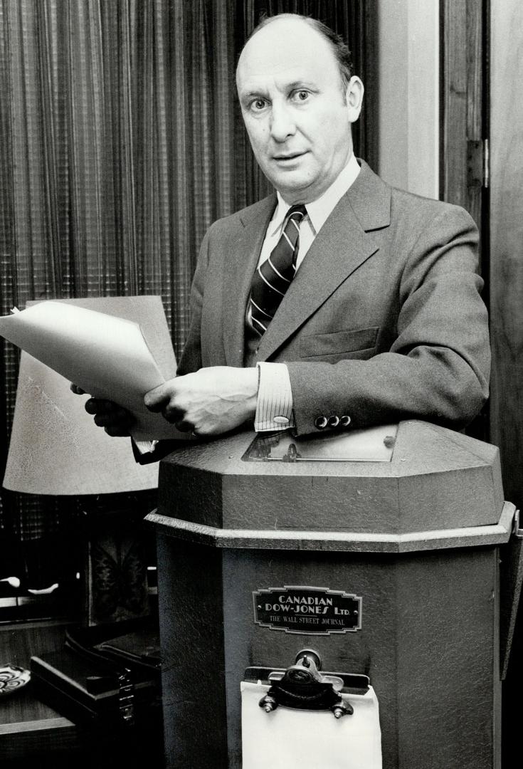 Michael Curry, new chairman of the Toronto Stock Exchange, poses with old Dow Jones machine which is now part of his office decoration. He is also deputy chaiirman of Walwyn Stodell Cochrane Murray Ltd., a top investment firm.