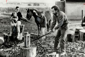 Foreman John Evanoff runs wood business part time, Wife Gaynor, daughters Missy, 1, Joanne, 10, watch him at work with axe.