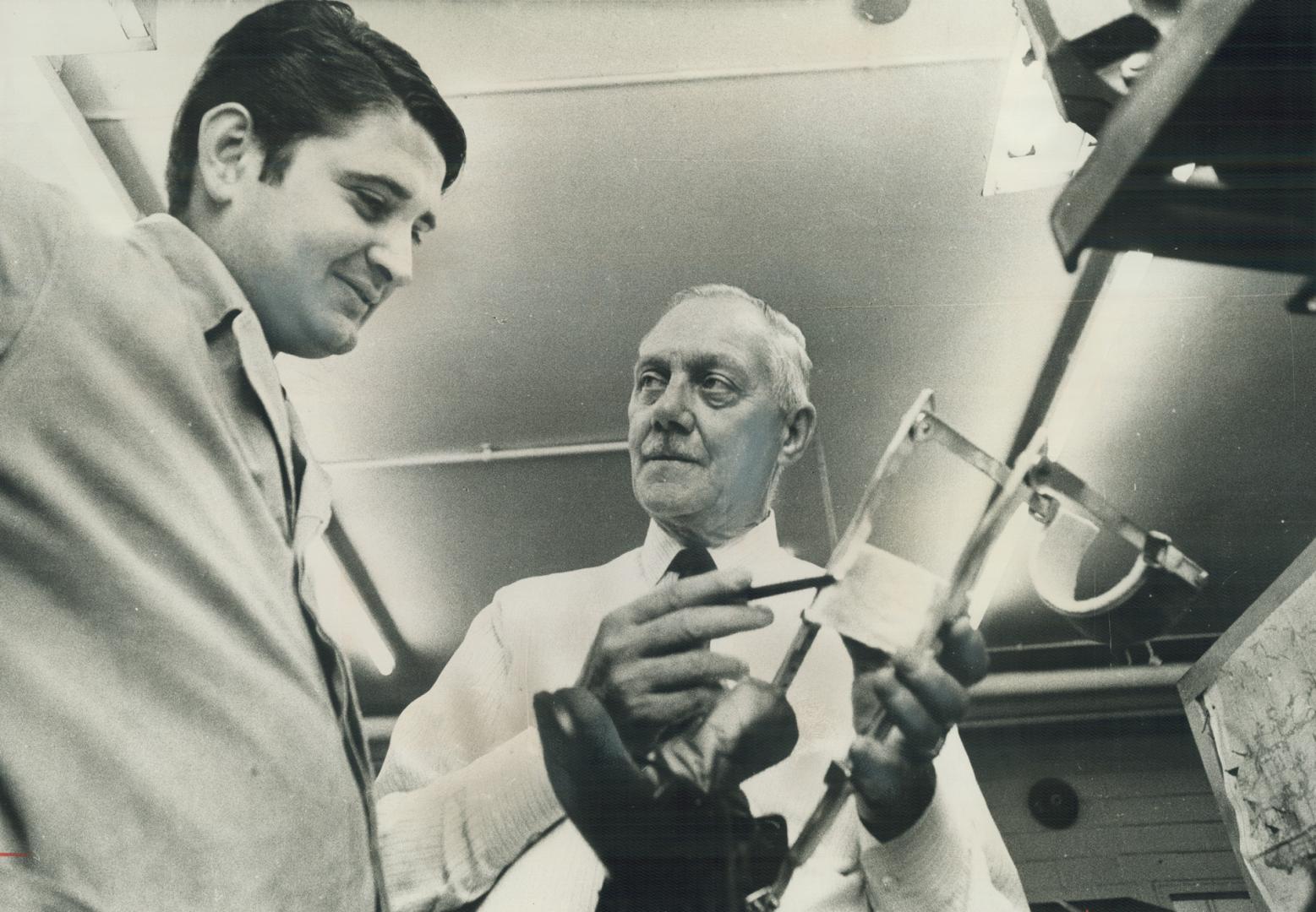 Blacksmith Albert Foster (right) discusses a leg brace being made in the basement machine shop at the Hospital for Sick Children, with Boris Mozetich Last year, he and his 12 workmen produced 7,000 special items orthopedic shoes, iron lugns, surgical tool