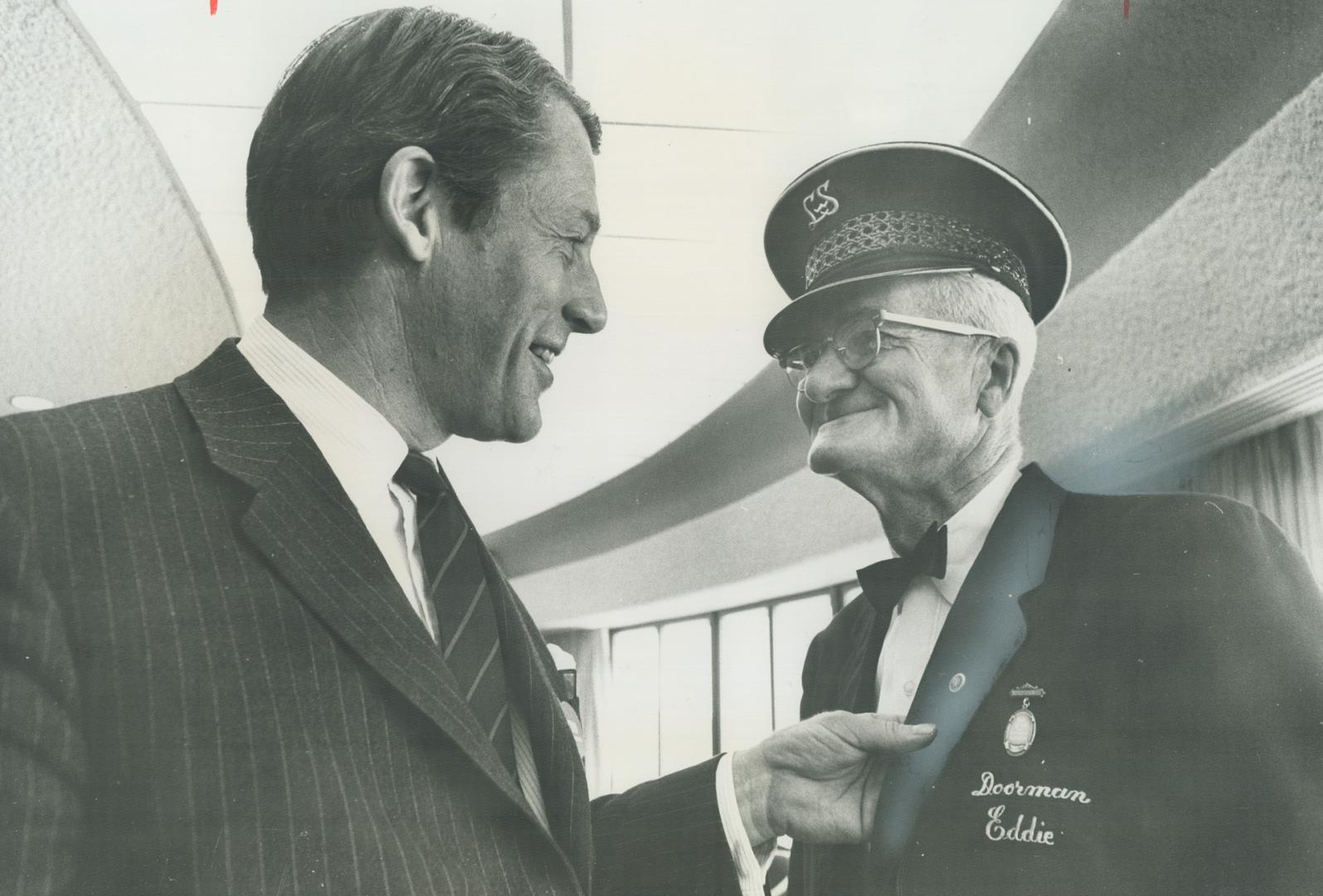 Mr. Ambassador for Metro's Welcome a Visitor Week, Eddie James Grogan, doorman at the Lord Simcoe Hotel, is congratulated by James Auld, Ontario minister of tourism and information, who pinned a silver medal on his chest for the style he uses in making visitors feel right at home.