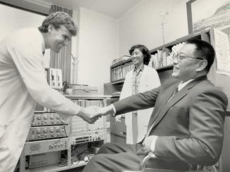 Friendly exchange: Deng Pufang, in wheelchair right, shakes hands with Dr. David Houlden of Sunnybrook Medical Centre who created machine to diagnose extent of spinal cord injuries. Deng, founder and director of the China Fund for the Handicapped, is on North American tour.