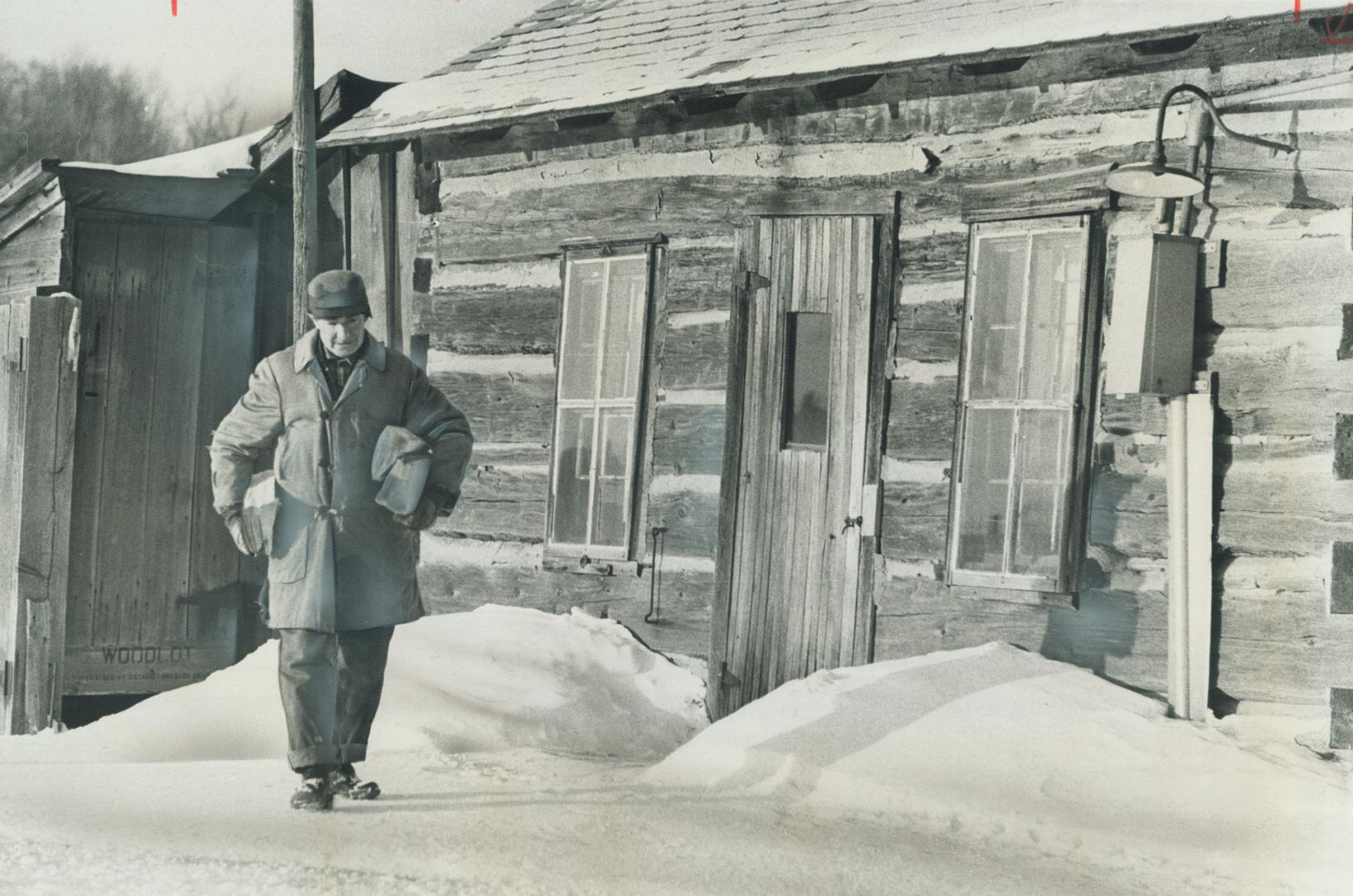 Carrying wood for his stove, 70-year-old John Lloyd walks in the yard in front of his log cabin home near Palgrave