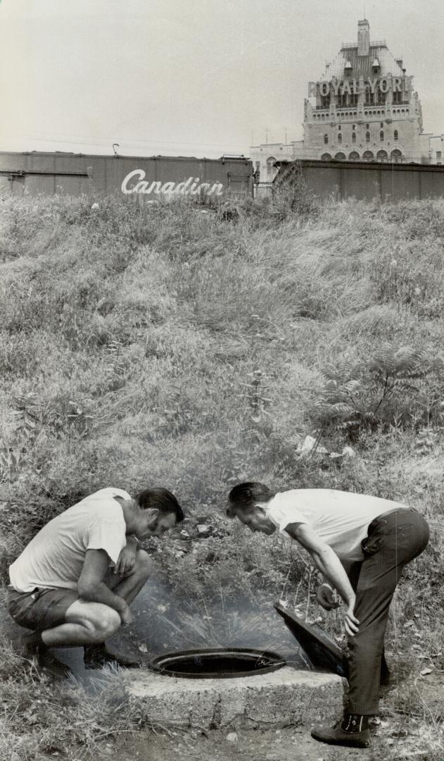 Manhole was home: Chris Conway and Ken Smart, parcel post drivers, peer into the manhole that was 54-year-old Svetomir Kusmanovich's home for three years