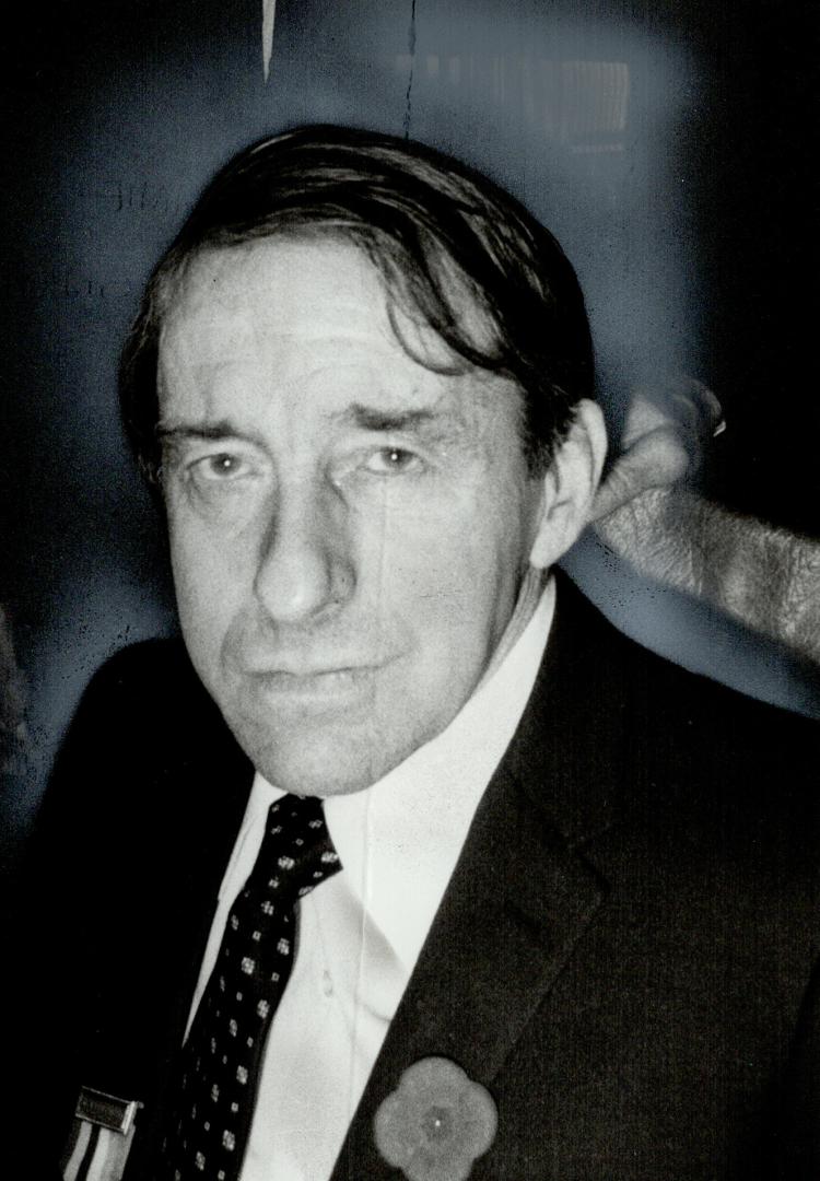 A closeup of a man, wearing a poppy in one lapel and a medal on the other.