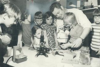 Amateur Geologist Harold Moran gives Alison Hokkanen, a Grade 3 pupil at Howard School, a look through his microscope at azurite rock samples in the science display he and his wife have set up in the school library this week