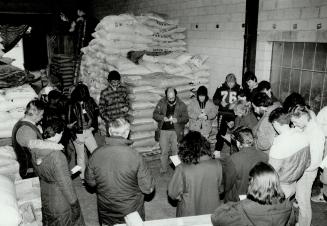 Work is blessed: Dr. Andrew Simone, centre, leads volunteer members of Canadian Food For Children in prayer yesterday before they start packing the piled-up foodstuffs for shipment to a mission in Uganda. Earlier this week, the organization sent food and medicines to Canadian nurse Theresa Hicks, who runs a clinic in a squatters' camp in Liberia.