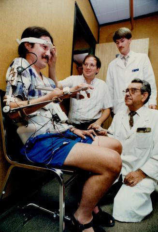 Richard Smith has blink machne adjusted by Isaac Kurtz, as Mendal Slack, standing, and Leslie Szendi look on.