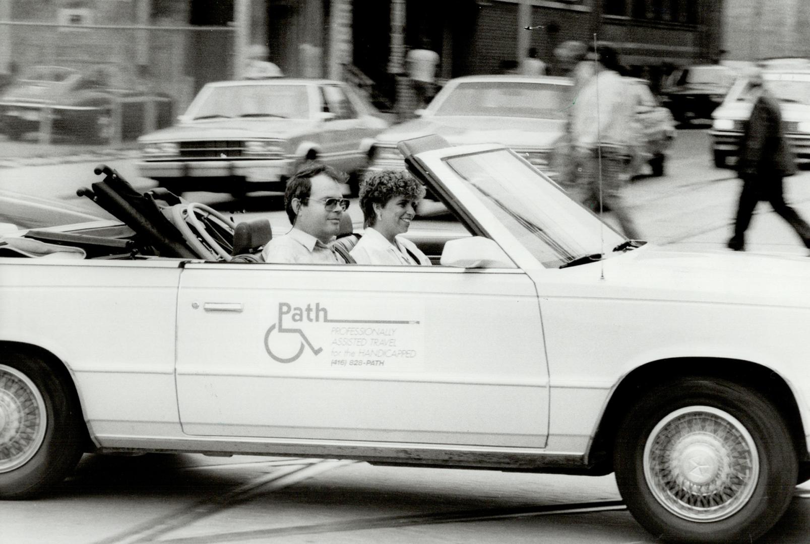 On the move: Quadriplegic Dave Tierney and nurse Debbie Reiss zip through downtown Toronto traffic in a convertible, advertising their travel service for the physically and mentally handicapped