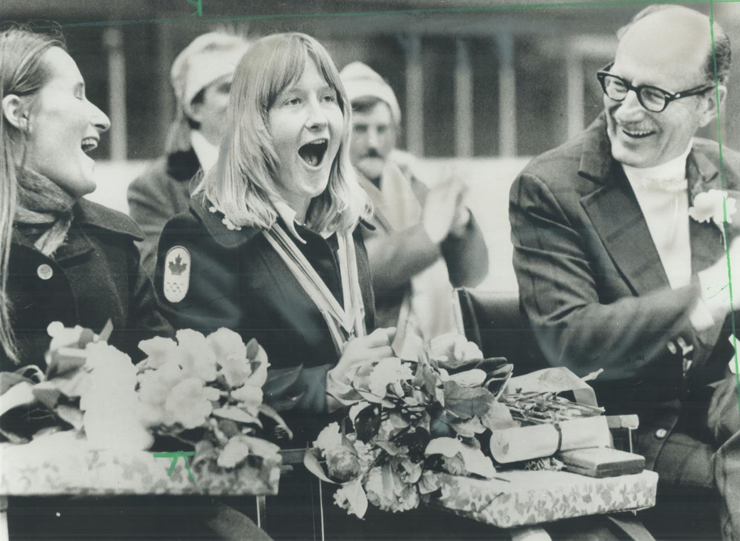 Back home in Timmins with Canada's only first-place gold medal from the Winter Olympics, skier Kathy Kreiner is applauded by her father, Dr. Harold Kreiner (right), and 1,000 other people in the Community Sportsplex. About 200 well-wishers greeted her at the tiny Timmins airport, others lined the seven-mile road into town. Kathy surprised the ski world by winning the women's giant slalom.