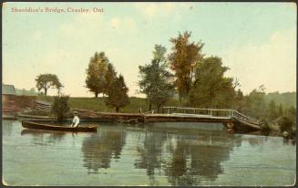 Person in a canoe on a smaller river, with small log bridge in the background.