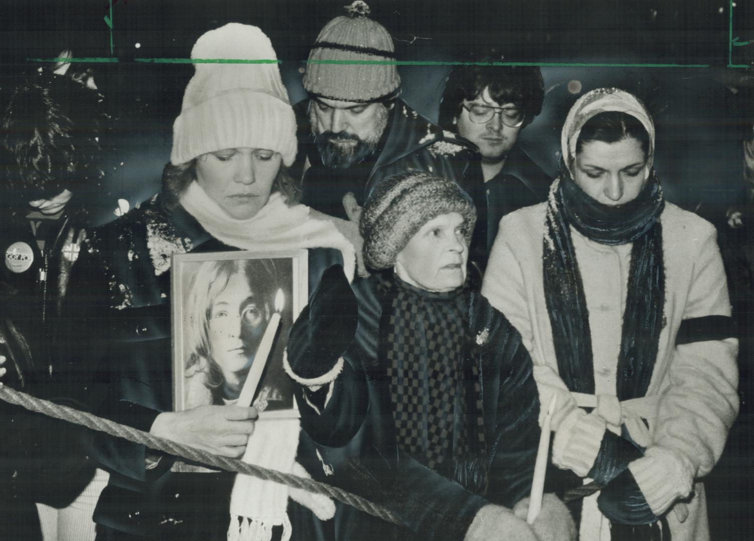 Last respects: Frieda Vanderbelde, 30, (left) is flanked by two unidentified mourners as she holds a picture of slain ex-Beatle John Lennon during last night's Nathan Phillips Square tribute