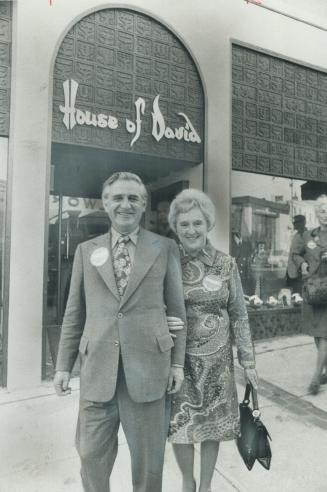 NDP leader David Lewis and his wife, Sophie, pass beneath a store sign in Guelph bearing his name-but not belonging to him-during tour in Guelph yesterday