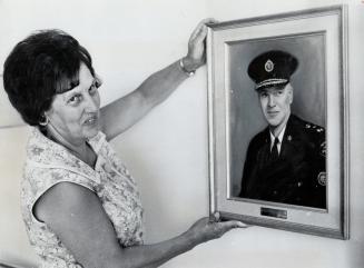 Mrs. James Mackey adjusts her husband's portrait. The Mackeys recently moved, and she's busy putting the new apartment in order