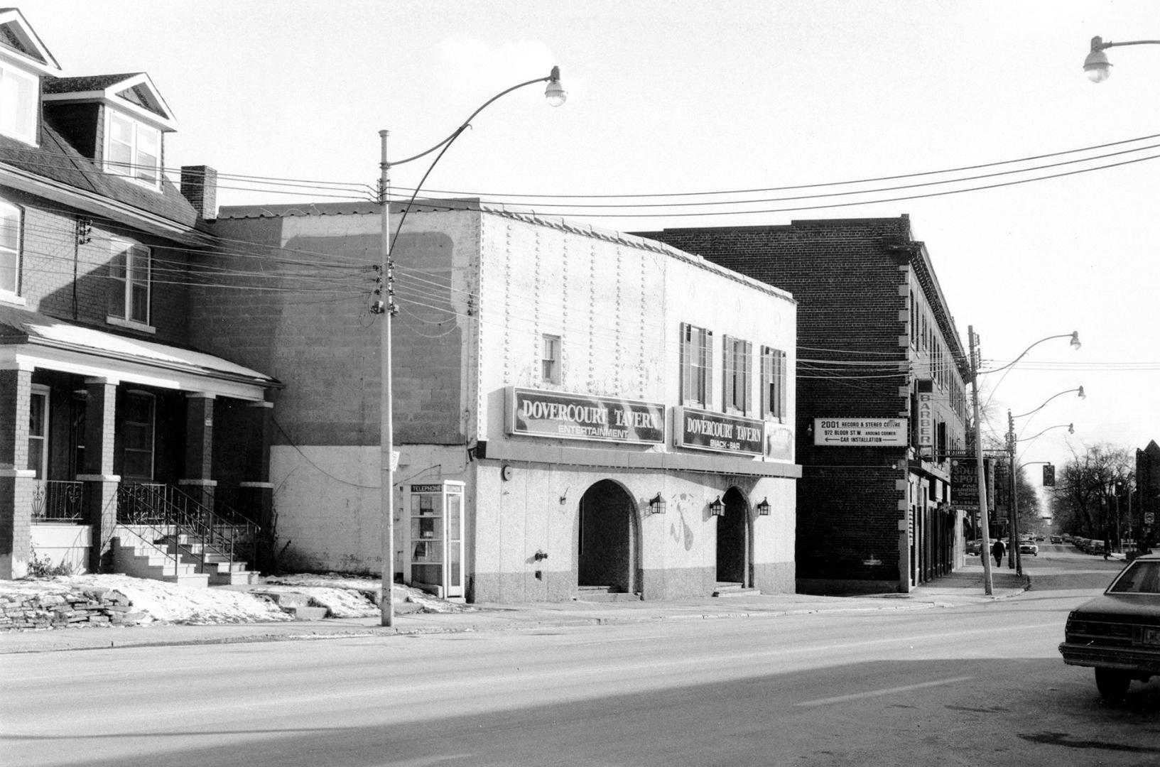 A two-storey square white brick building with very few windows. Two large signs over two arched ...