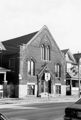 Taken from across the street, the photo shows a three-storey church-like building, with arched …