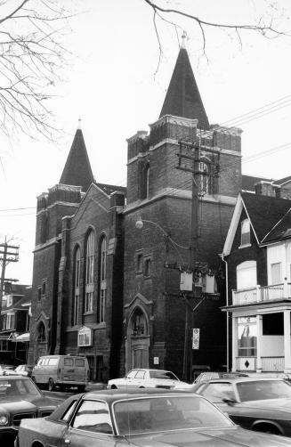 Photo taken across the street, of a church with two towers, both with arched doorways, crenella…