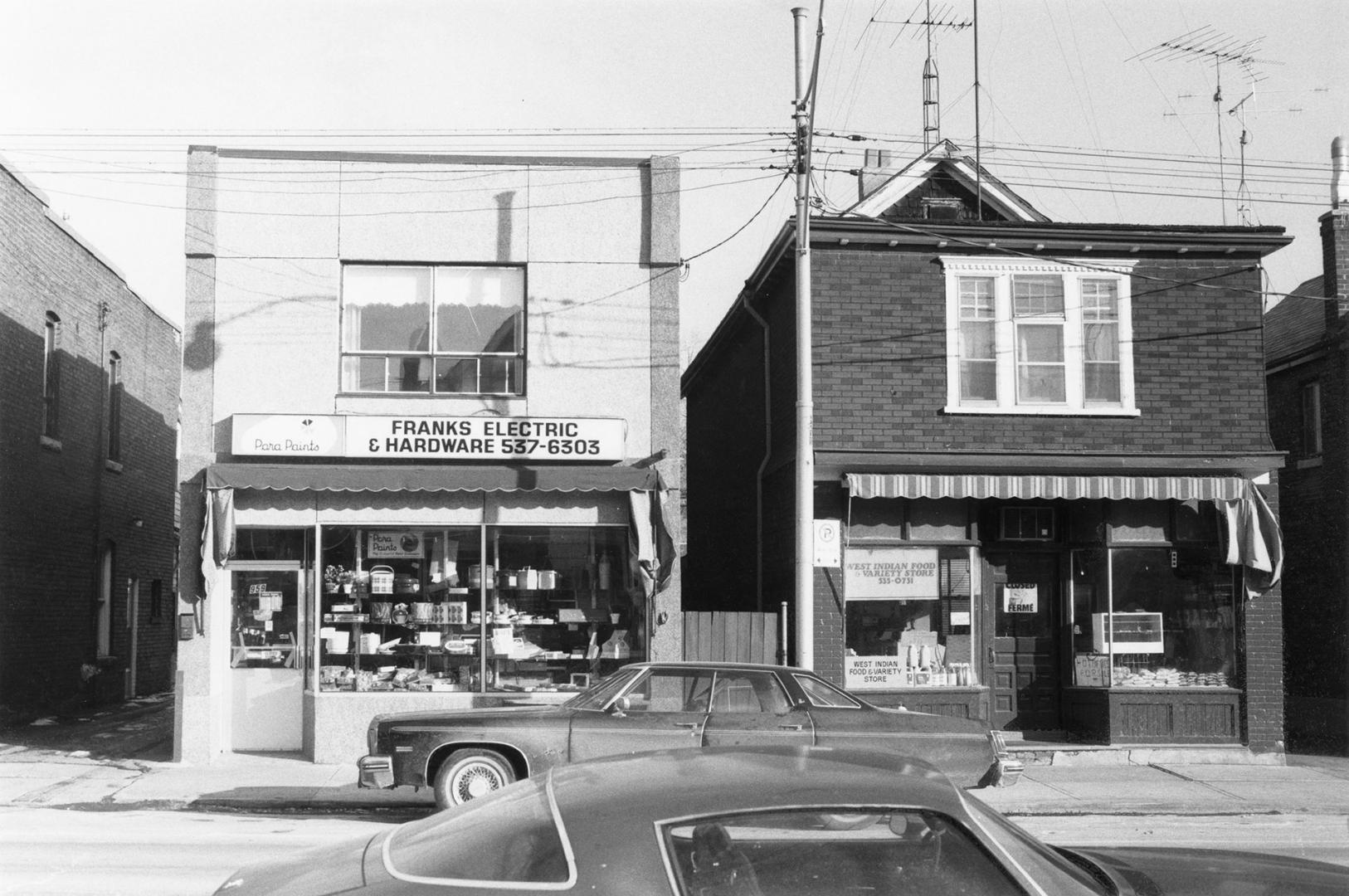 A photo, taken across the street from two shops with apartments above them. The one on the left…