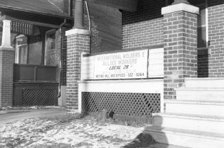 Detail of a house with a wooden staircase. On the porch, a sign reads International Molders E A ...