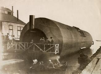 Image shows a few people looking inside the roller boat and some are on a small boat beside it.