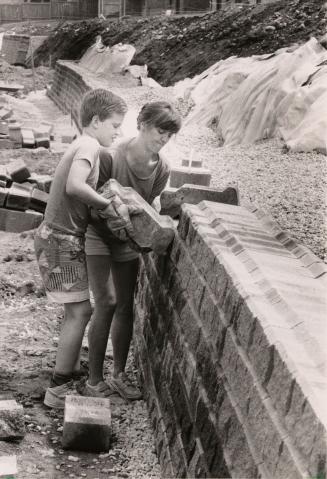 Stephen Gilbert helping mother Linda hoist part of a retaining wall. Ajax, Ontario