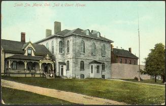 Three adjoining buildings. On the left, a 2-storey wood house with gingerbread trim. In the cen…