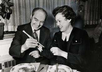 Rene Brunelle, minister of community and social services, get a lesson in using chopsticks from Edith Liu at the dinner of the Mon Shong Foundation last night