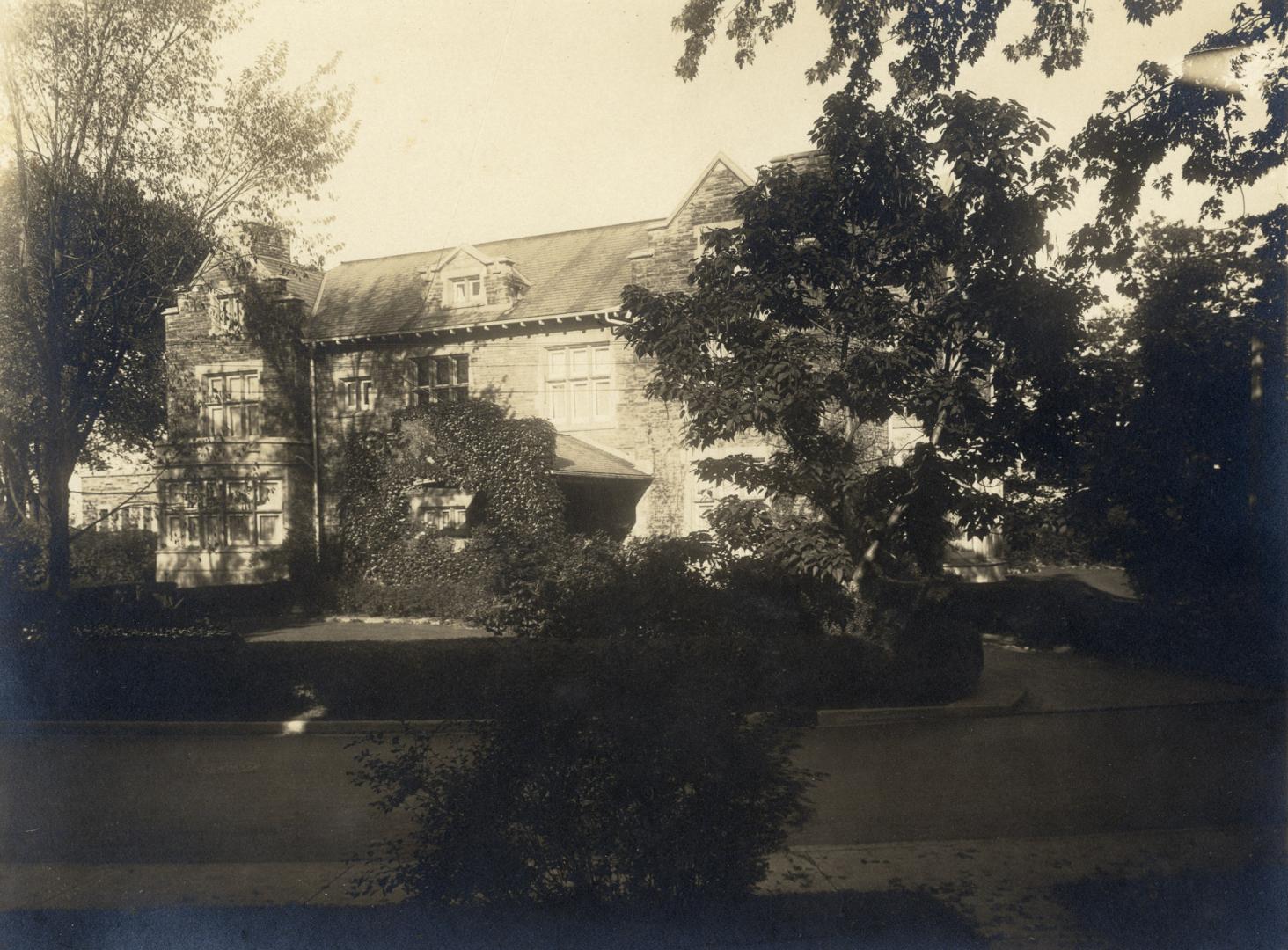 Image shows a limited view of a two storey residential house with a lot of trees around it.