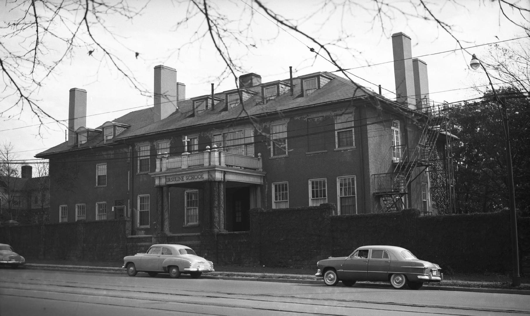 Image shows a two storey building with a few cars parked along the street.