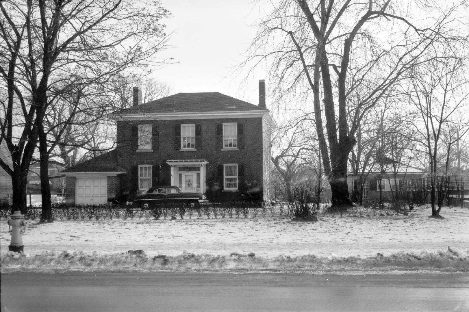 Image shows a two storey residential house with a car parked in front of it.