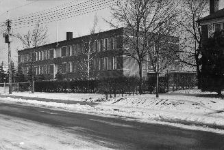 Image shows a street view with a two storey school building along it.