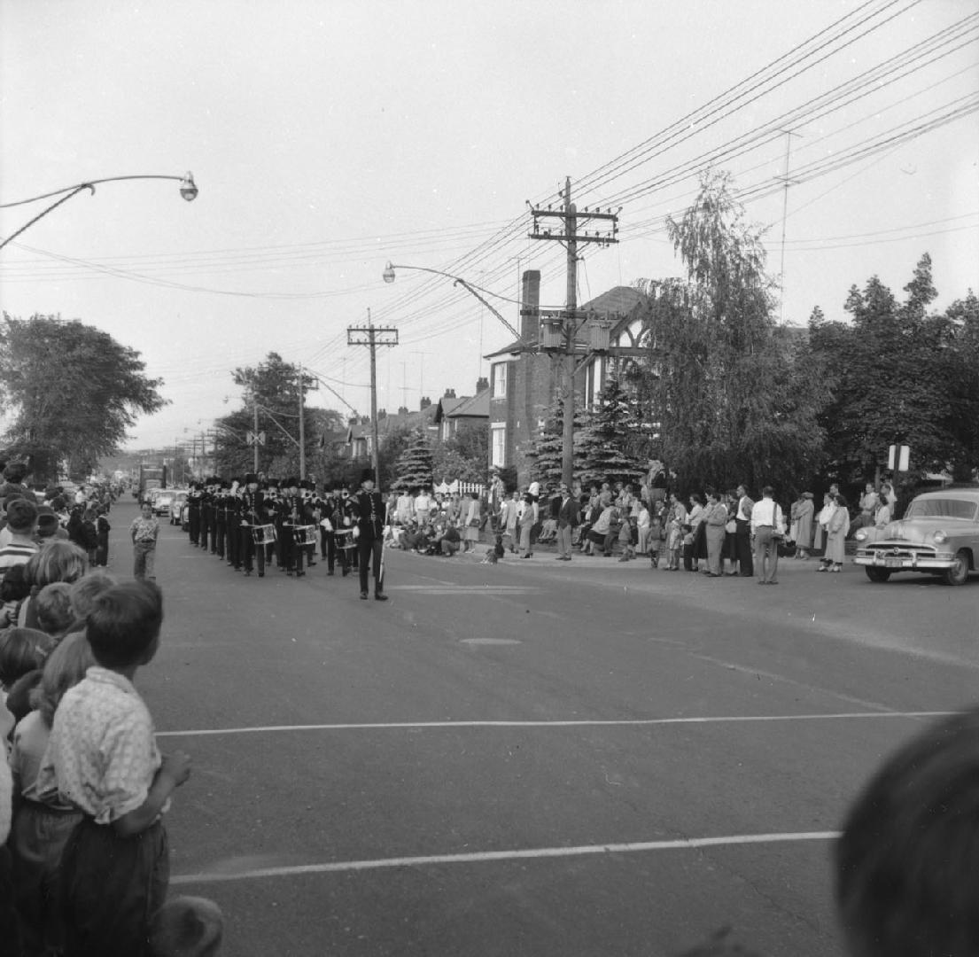 Image shows participants of the parade marching along the street with some spectators cheering …