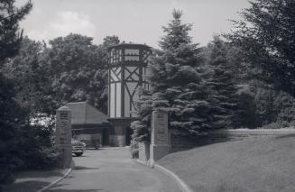 Image shows a road leading towards the open gates. Stables are seen in the background.