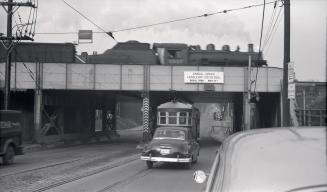 Image shows a street view with the CP rail bridge over it. 