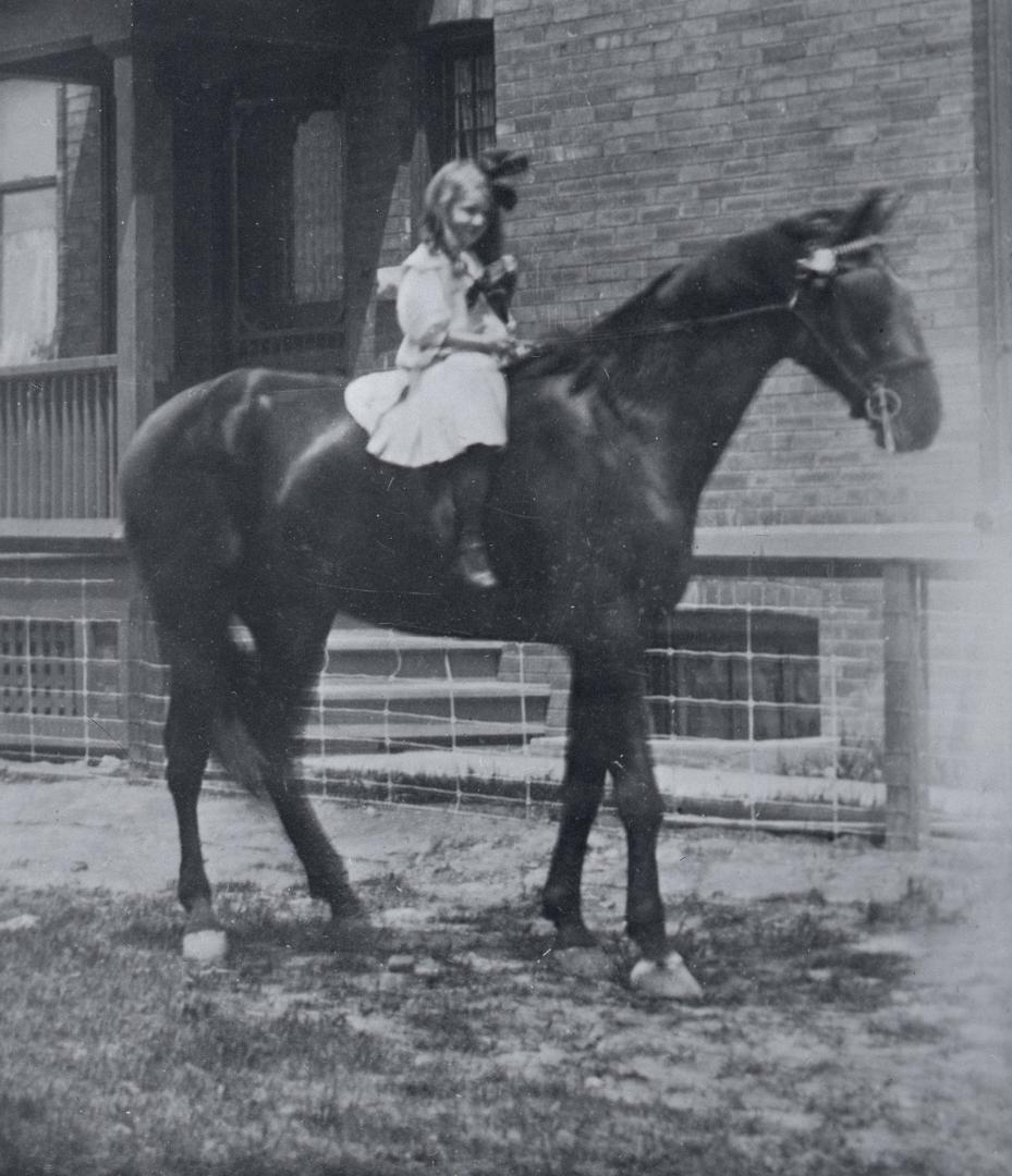 Image shows a girl riding a horse by the building.