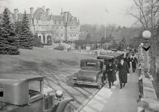 Image shows a few people walking on the sidewalk with a Government building in the background.