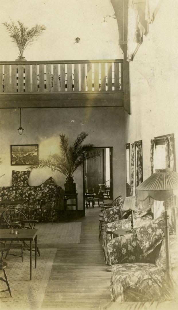 Image shows an interior with some couches, tables, chairs and palm trees.