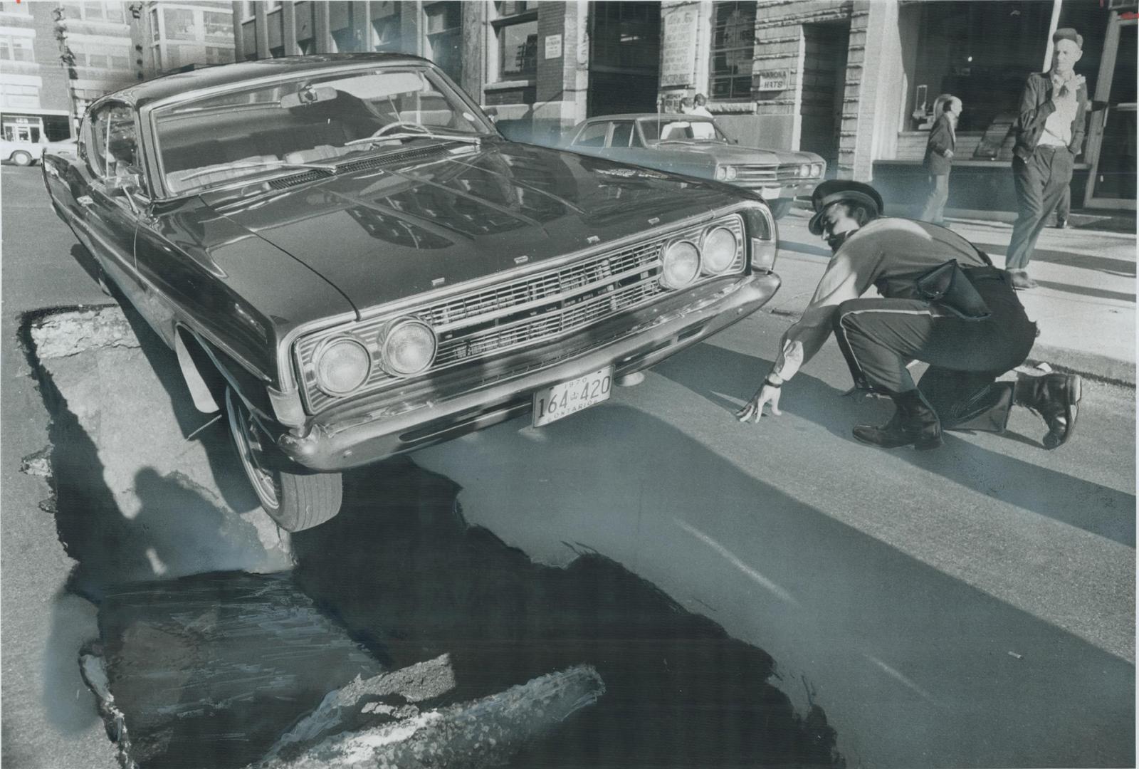 When the pavement caved in. Constable Anthony Pietranio kneels to look for damage to car balanced over cave-in on Camden St., a short street in Spadin(...)