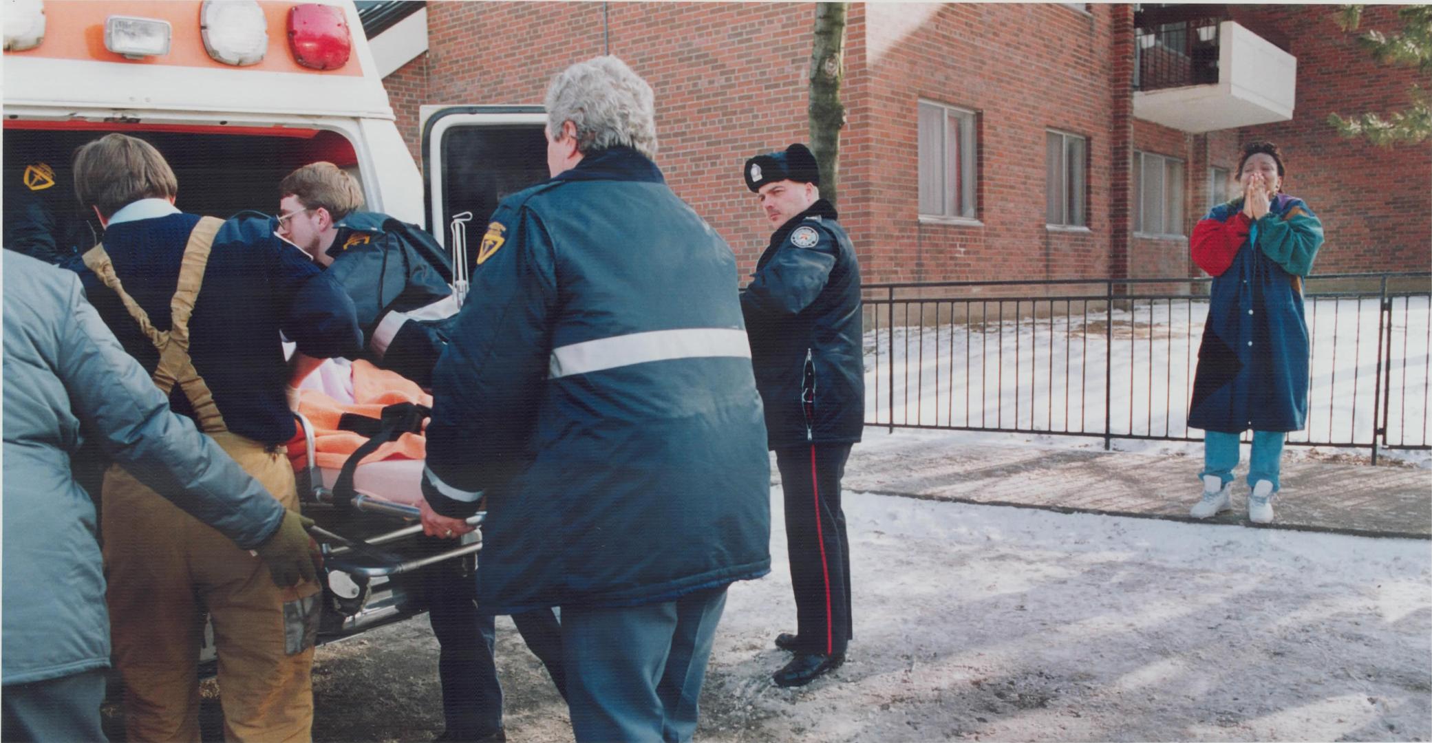 A distraught woman whose infant daughter and granddaughter drowned in a bathtub watches as one of the victims is placed in an ambulance