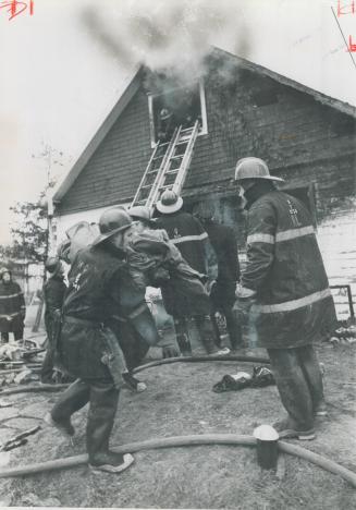 Blanket-shrouded body of one of six dead children of Lumsden family is carried by firemen to waiting ambulance